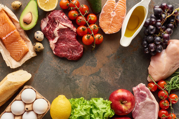 Вид сверху сырой рыбы, мяса и птицы рядом с овощами, фруктами, яйцами, зеленью, багетом и оливковым маслом на мраморной поверхности с копировальным пространством
