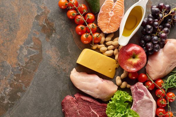 Top view of raw fish, meat and poultry near vegetables, fruits, cheese, peanuts, herb and olive oil on marble surface with copy space