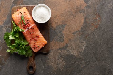 top view of raw salmon with peppercorns, parsley and salt on wooden cutting board clipart