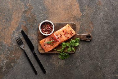 top view of raw fresh salmon with peppercorns, parsley on wooden cutting board near cutlery clipart