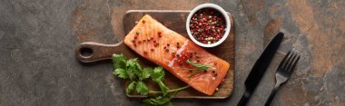 top view of raw fresh salmon with peppercorns, parsley on wooden cutting board near cutlery, panoramic shot clipart