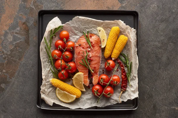 top view of raw salmon with vegetables, lemon and rosemary in oven tray