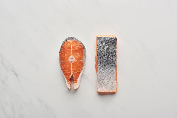вид сверху на сырые свежие стейки лосося с рыбными чешуями на поверхности белого мрамора
