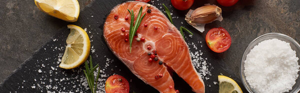 top view of raw salmon steak with salt, lemon and tomatoes on stone board, panoramic shot