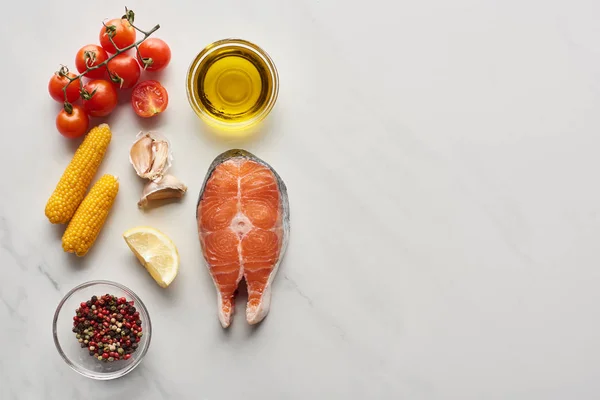 Top view of uncooked salmon steak near lemon, corn, tomatoes, garlic, oil and peppercorns in bowls on marble table — Stock Image Top View Uncooked Salmon Steak Lemon Corn Tomatoes Garlic Oil Stock Picture