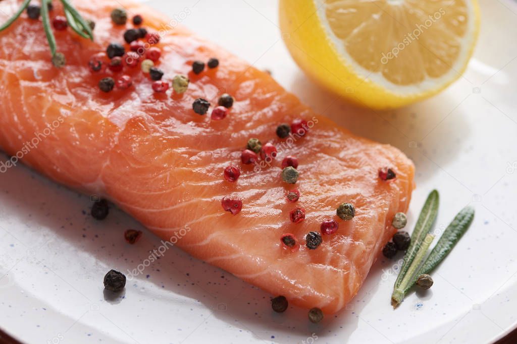 close up view of raw fresh salmon with pepper, lemon and rosemary