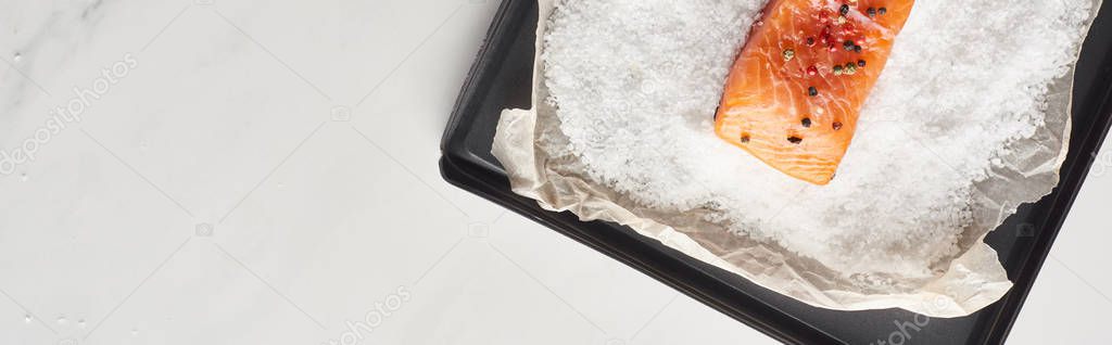 top view of raw salmon steak with pepper on oven tray with salt on marble surface, panoramic shot