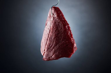 raw beef sirloin on hook on dark black background clipart