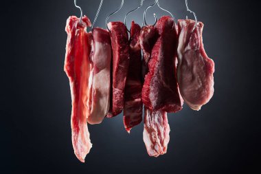 koyu siyah arka plan üzerinde metal kancalar üzerinde çeşitli çiğ et biftek ve pastırma