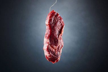 raw beef fillet on metal hook on dark black background clipart