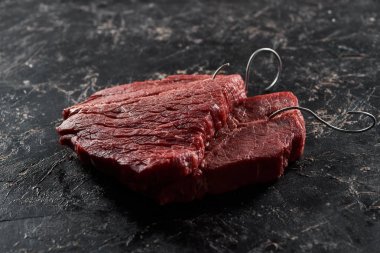siyah mermer yüzeyinde metal kancaile çiğ sığır biftek