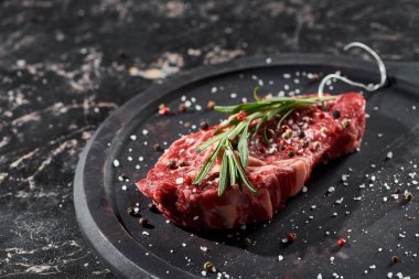 raw meat steak with rosemary twig sprinkled with salt and pepper on round wooden surface clipart