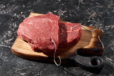 wooden cutting board with raw beef steaks on black marble surface clipart