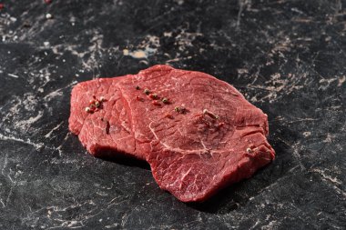 raw beef steak sprinkled with peppercorns on black marble surface clipart