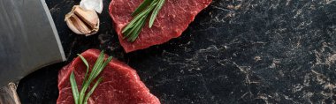 panoramic shot of unprocessed beef steaks with rosemary sprigs near garlic and knife on black marble surface clipart