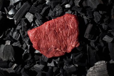 top view of raw beef steak on charcoal pieces clipart