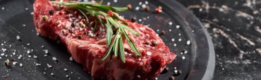 panoramic shot of raw beef fillet with rosemary twig sprinkled with salt and pepper on round wooden surface clipart