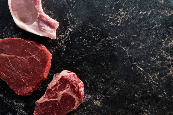 top view of raw beef and pork parts on black marble surface