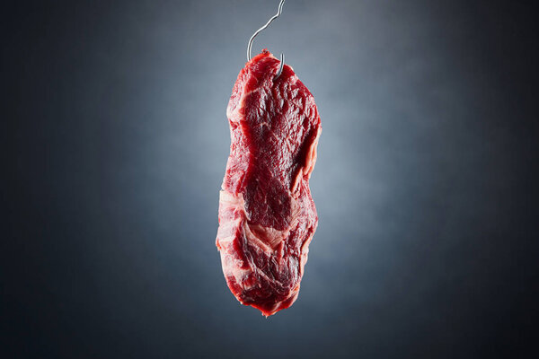 raw beef fillet on metal hook on dark black background