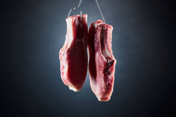 raw pork pieces on metal hooks on dark black background