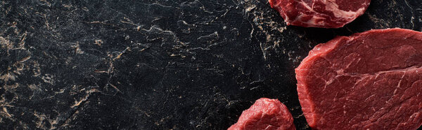 panoramic shot of several raw beef steaks on black marble surface