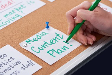 cropped view of woman writing media content plan inscription on card pinned on cork board clipart