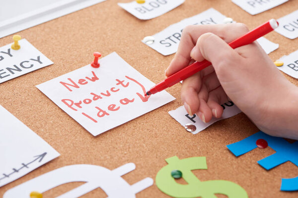 cropped view of woman holding red felt-tip pen near card with new product idea inscription on cork board