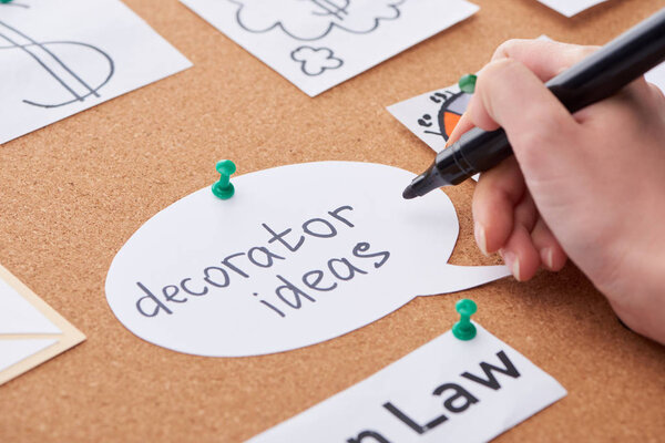 cropped view of woman holding black highlighter near blank with decorator ideas inscription pinned on cork board