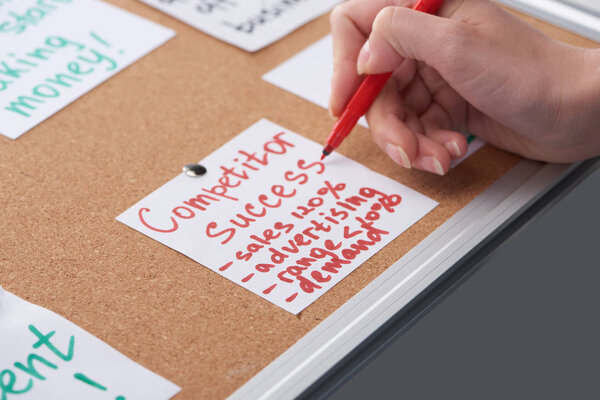 cropped view of woman writing competitor success notes on card pinned on cork board