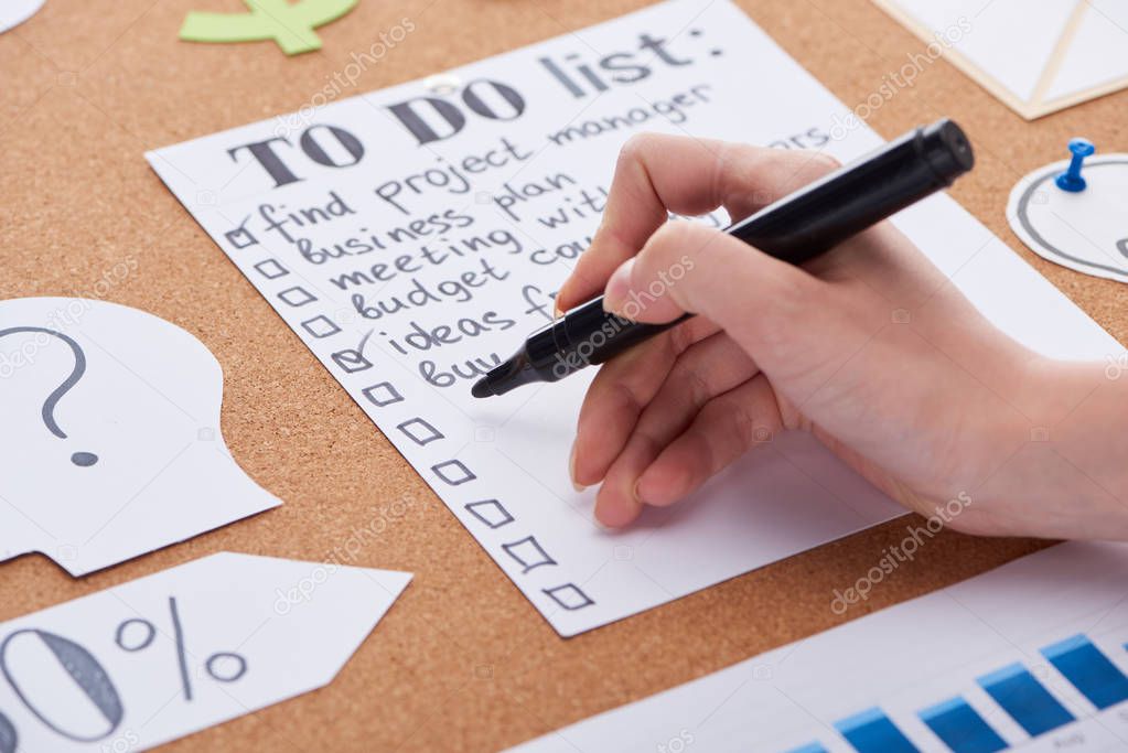 cropped view of woman writing with black highlighter on to do list on cork board