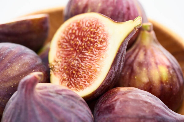 close up view of ripe delicious fig half in wooden bowl on white background