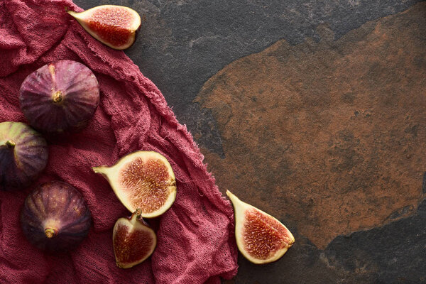 top view of ripe whole and cut delicious figs on rustic red cloth on stone background