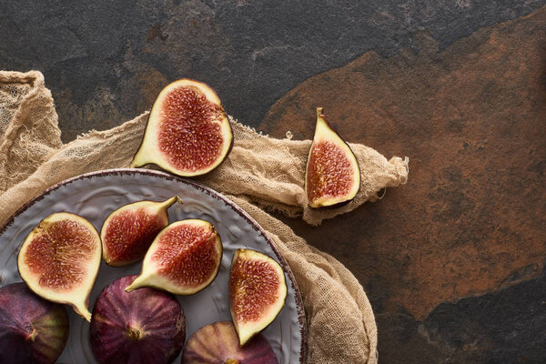 top view of ripe figs on white plate with rustic cloth on stone background
