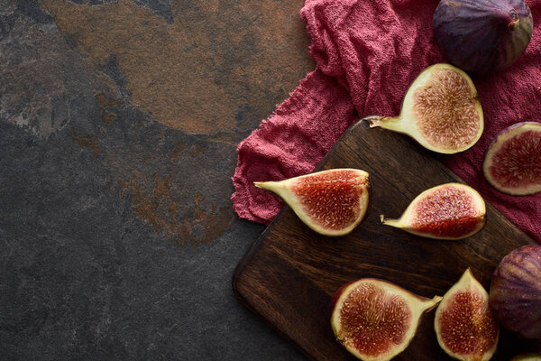 top view of ripe figs on wooden cutting board near red cloth on stone background