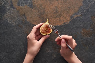 cropped view of woman holding fork and ripe delicious fig half on stone background clipart
