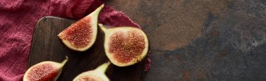 panoramic shot of ripe cut figs on wooden cutting board on red cloth on stone background clipart