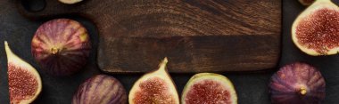 panoramic shot of ripe figs around wooden cutting board on stone background clipart