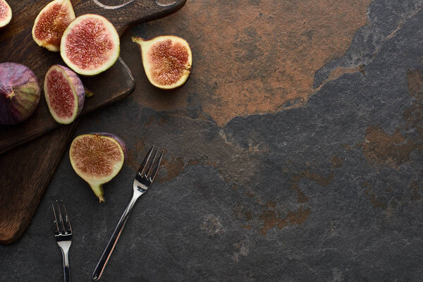top view of ripe whole and cut delicious figs on stone background with forks and cutting boards