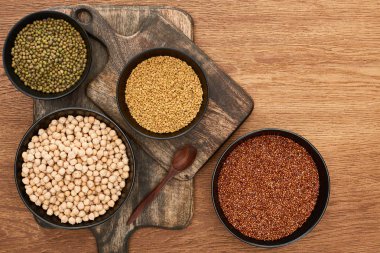 top view of bowls with moong beans, buckwheat and chickpea near spoon on wooden cutting boards clipart