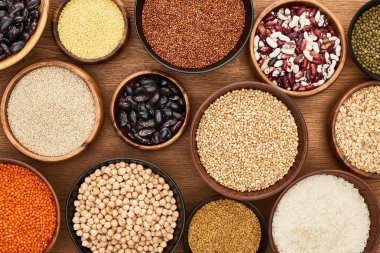 top view of bowls with whole grains and legumes on wooden surface clipart