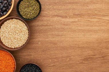 top view of bowls with black and moong beans, buckwheat and red lentil on wooden surface clipart