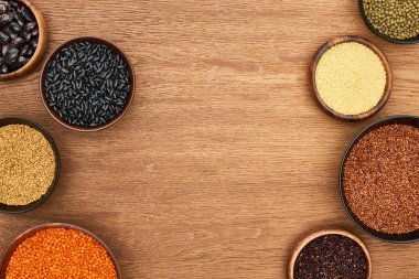 top view of bowls with quinoa, couscous, beans, chickpea and lentil on wooden surface clipart