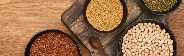 panoramic shot of bowls with roasted buckwheat, chickpea and beans near wooden spoon on wooden cutting boards clipart