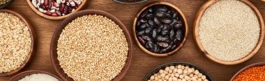 panoramic shot of bowls with oatmeal, buckwheat, quinoa, beans and chickpea on wooden surface clipart