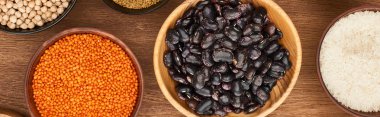 panoramic shot of bowls with red lentil, black beans, white rice and chickpea on wooden surface clipart