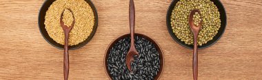 panoramic shot of bowls with diverse beans and grains with spoons on wooden surface clipart