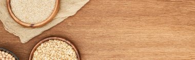 panoramic shot of bowls with oatmeal, chickpea and white quinoa on wooden surface with canvas clipart