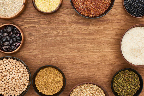 top view of bowls with beans, white rice, couscous and buckwheat and chickpea on wooden surface