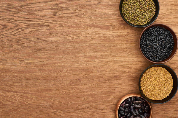 top view of bowls with black beans, maash and buckwheat on wooden surface