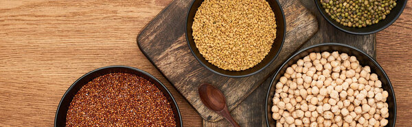 panoramic shot of bowls with roasted buckwheat, chickpea and beans near wooden spoon on wooden cutting boards